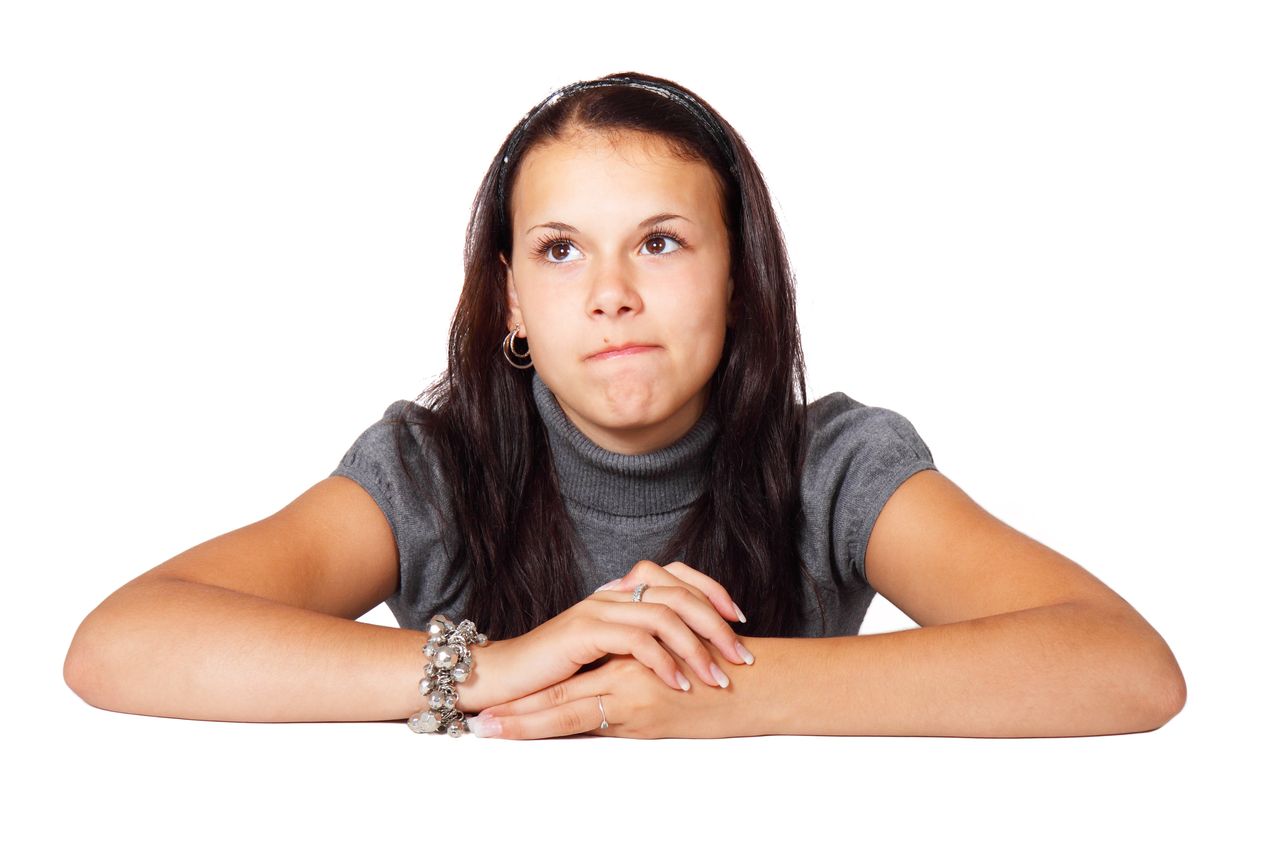 A young woman with a pensive expression sits thoughtfully against a white background, conveying introspection.