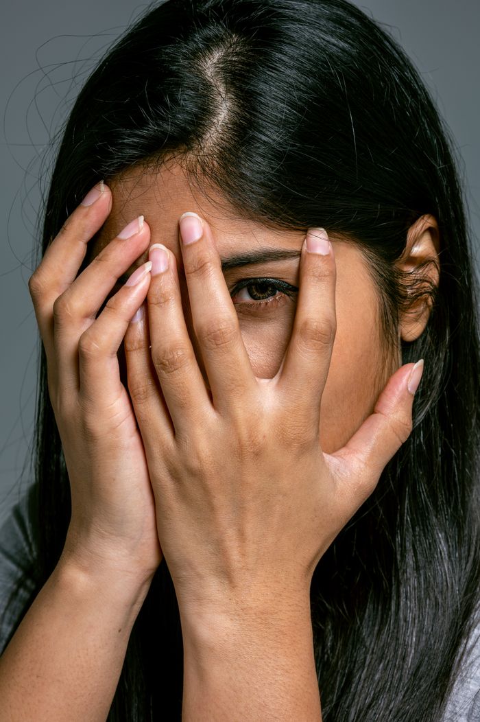 Close-up of a woman covering her face with hands, expressing emotions and conveying a sense of stress or sadness.